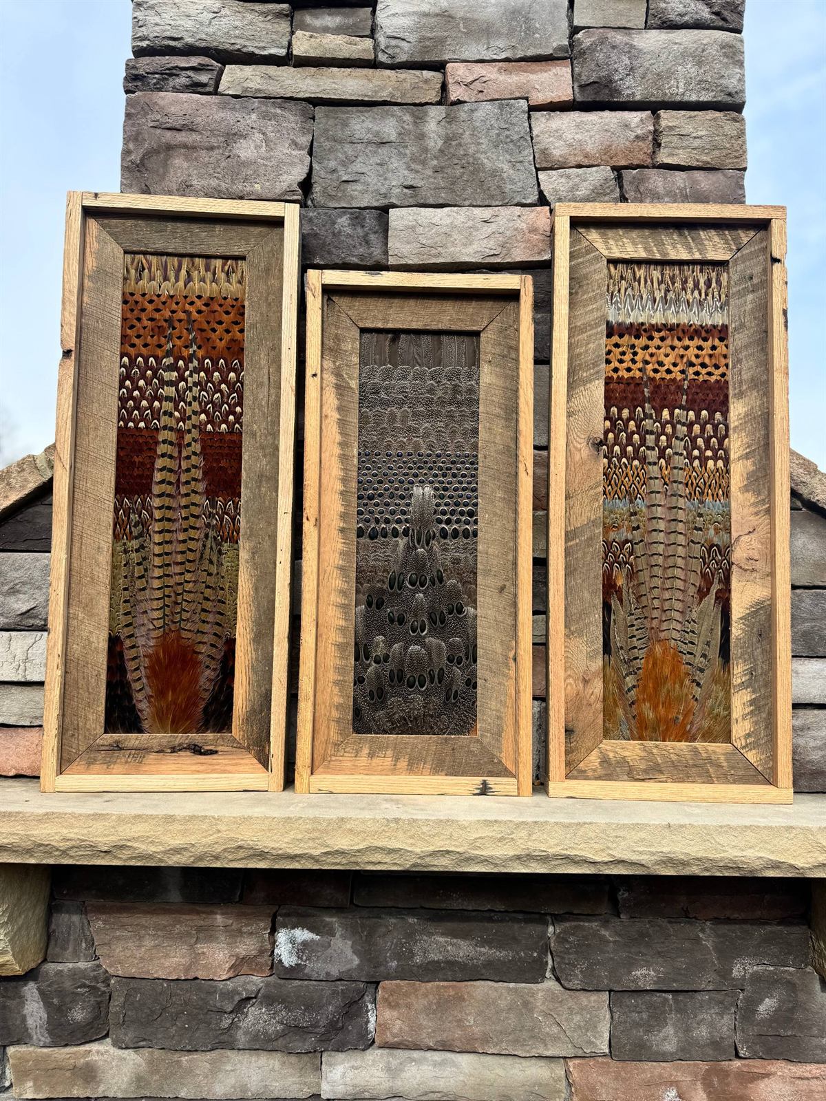 Triptych of upland feather panels in reclaimed oak, staged on an outdoor stone fireplace